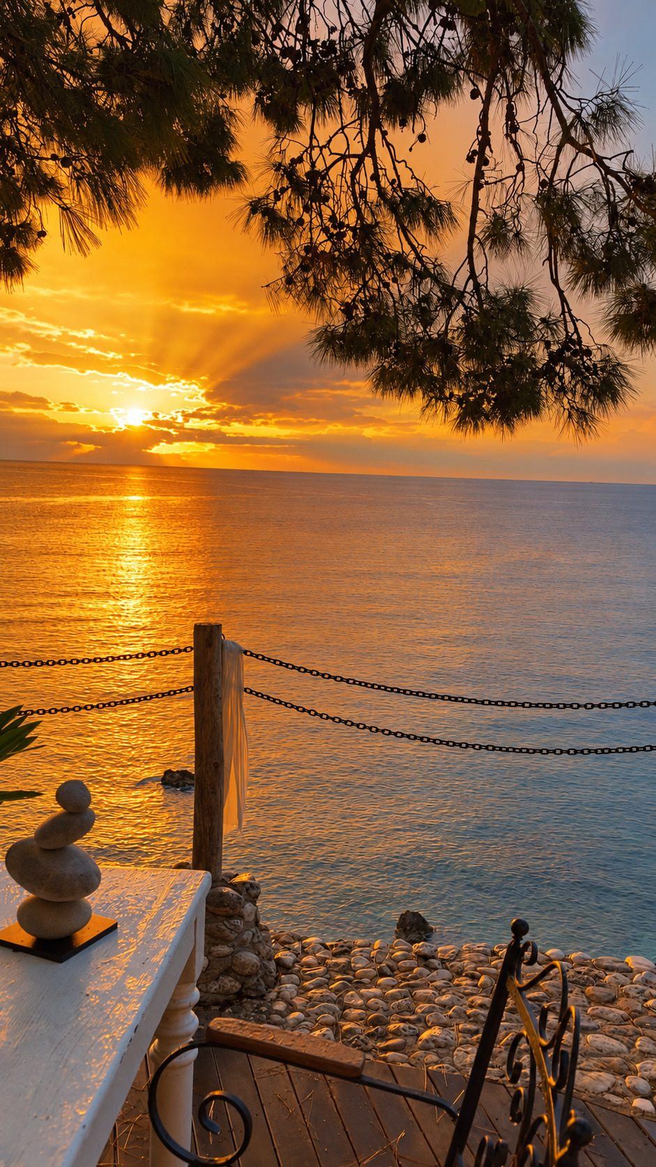 Atardecer sobre el mar visto desde una terraza con una baranda de cuerdas y piedras apiladas.